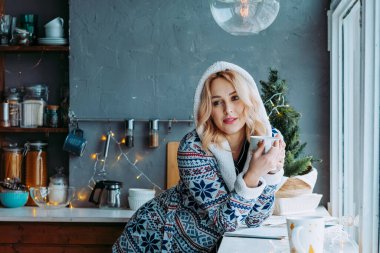 Pijamalı kız pencerenin yanında kahve içiyor. Evde pijamalı sabah kahvesi. Kız elinde bir fincanla düşünceli bir şekilde pencereden dışarı bakıyor. Dur ve düşün.