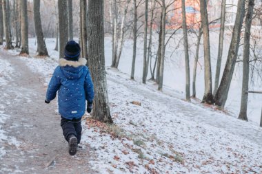 Çocuk kış ormanında yürüyor. Soğuk ülkelere seyahat etmek. Bir çocuk ormanda bir patika boyunca yürür. Doğa yürüyüşü