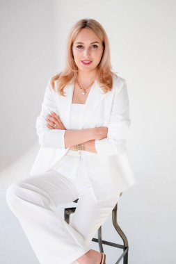 Beyaz arka planda kendine güvenen genç ve güzel bir yönetici. Beyaz takım elbiseli sarışın kız beyaz arka planda, bir sandalyede oturuyor. Güçlü ve bağımsız bir iş kadını. Güçlü bakışlı güzel bir kız. Pantolon giymiş şık bir kız.