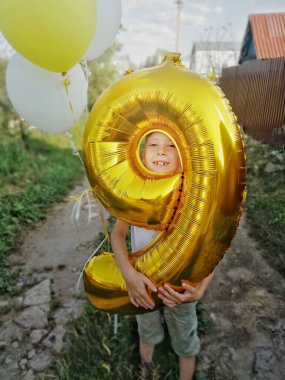 Çocuk 9 numarayı tutuyor. Balonlu bir çocuğun doğum günü. Doğumgününde doğada bir çocuğun komik bir fotoğrafı. Yazın doğum günü