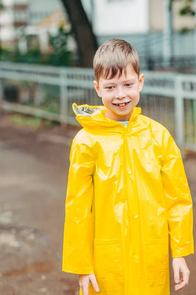 A boy in a yellow raincoat walks outside in the rain. Beautiful and smiling child on the street. portrait of a boy of European uncomfortableness. Open smile of a child