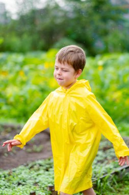 Sarı yağmurluklu bir çocuk yağmurda dışarıda yürür. Sokaktaki güzel ve gülümseyen çocuk. Parlak kıyafetler. Yağmurda yürü.