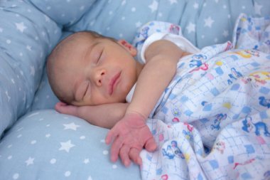 Sweet calm newborn baby sleeping on the bed with hand under his cheek