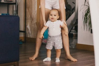 Erkek bebeğin ilk adımları. Küçük çocuk yürümeyi öğreniyor. Anne oğlunun yürümesine yardım eder.