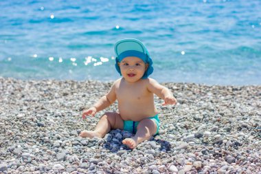 Çakıl taşlı sahilde tatlı tombul bebek. Mavi deniz ve yaz güneşi