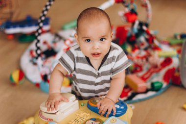 Şirin tombul bebek ayakta duruyor ve çocukların müzik sehpasıyla oynuyor. Her yerde bir sürü renkli oyuncak var..