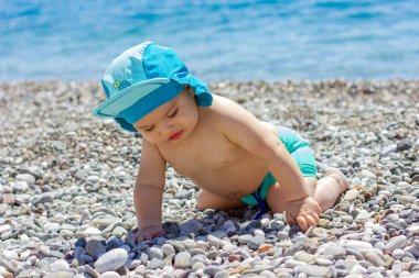 Çakıl taşlı sahilde tatlı tombul bebek. Mavi deniz ve yaz güneşi