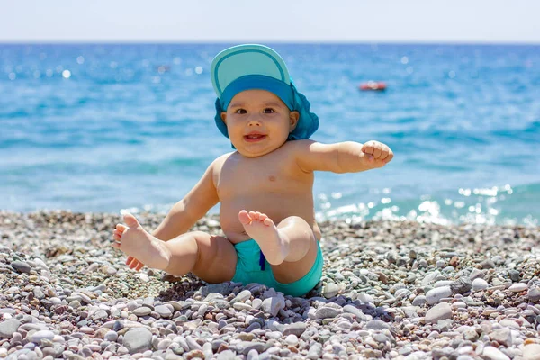 Çakıl taşlı sahilde tatlı tombul bebek. Mavi deniz ve yaz güneşi