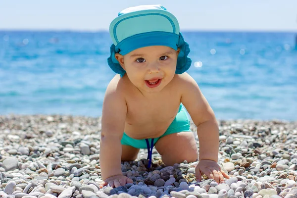 Sweet chubby baby on pebble beach. Blue sea and summer sunshine