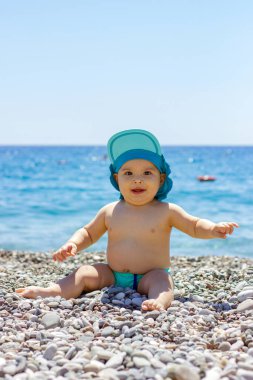 Çakıl taşlı sahilde tatlı tombul bebek. Mavi deniz ve yaz güneşi