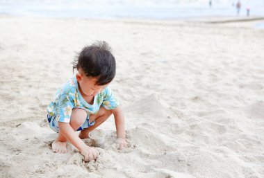 Küçük Asyalı çocuğun plajda kumla eğlenen portresi..