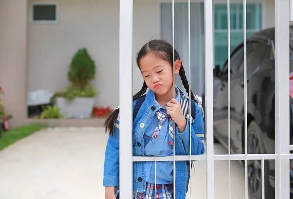 早上上学前 穿着幼稚园制服的亚洲小女孩在家门口的篱笆边 脸上挂着滑稽的表情 — 图库照片