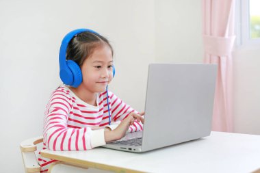 Evde yeni normal Covid-19 Coronavirus sırasında öğretmeniyle bilgisayardan bilgisayar kullanarak kulaklık eğitimi alan Asyalı küçük kız.