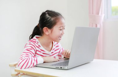 Çekingen Asyalı küçük kız masada oturuyor ve dizüstü bilgisayar kullanıyor. Evde kal.