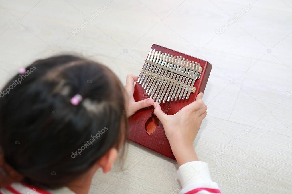 Close-up Asian young hands playing Kalimba (Mbira or thumb piano) lying on wood floor at home. Rear view