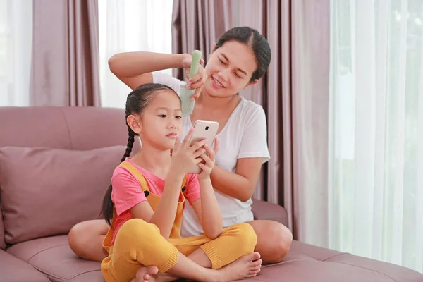 Aziatische Mam Kammen Haar Voor Haar Dochter Terwijl Spelen Smartphone — Stockfoto