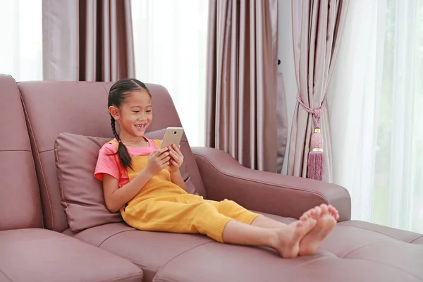 Menina Asiática Feliz Criança Enquanto Joga Smartphone Sofá Sala Estar — Fotografia de Stock