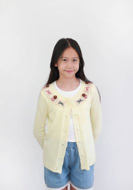 Sevimli sarı örülü hırka, çiçek desenli ve kot şortla poz veren neşeli genç bir kız çocuk modası ya da portresi için beyaz arka planda..