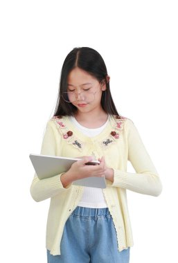 Pastel sarı işlemeli hırka ve gözlük giyen odaklanmış genç Asyalı kız, beyaz arka planda dikilirken dijital tablet kullanıyor..