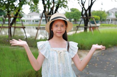 Hasır şapkalı ve yazlık elbiseli neşeli genç kız banliyö parkında ayakta duruyor, kollarını açık avuçlarıyla sanki güzel bir çevreyi sunuyormuş gibi açıyor..