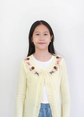 Dekoratif desenli kot pantolonlu, açık sarı hırkalı yakışıklı genç Asyalı kız beyaz arka planda izole edilmiş, nazikçe gülümseyen ve kameraya bakıyor..