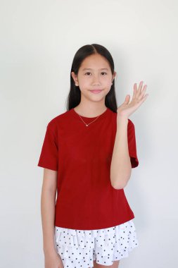 Kırmızı tişörtlü ve benekli etekli çekici Asyalı kız gülümsüyor ve beyaz arka planda dostça selamlaşarak elini sallıyor..