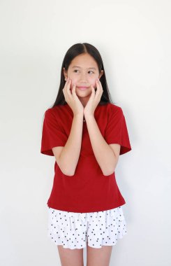 Elleri yanaklarında poz veren, beyaz arka plana karşı neşeli ve düşünceli bir ifadeyle bakan kırmızı tişörtlü tatlı Asyalı kız..