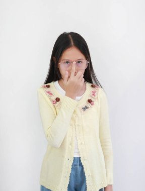 Asyalı kız altın çerçeveli gözlüğünü tek eliyle ayarlıyor açık sarı hırka giyiyor, beyaz arka planda dikkatlice kameraya bakıyor..