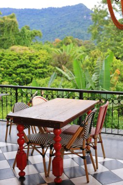 Boş bistro masaları ve dokuma sandalyeler sessizce bir balkonda oturur, davetlilerin yemyeşil tropikal ormanı ve uzak dağları gören bir yemeğin tadını çıkarmalarını beklerler..