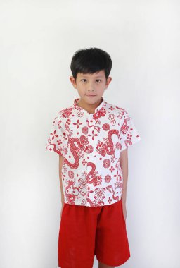 Yakışıklı Asyalı çocuk kameraya nazik bir gülümsemeyle bakıyor. Geleneksel beyaz bir gömlek giymiş. Ay Yeni Yılı kutlamaları için kırmızı ejderha resimleri var..