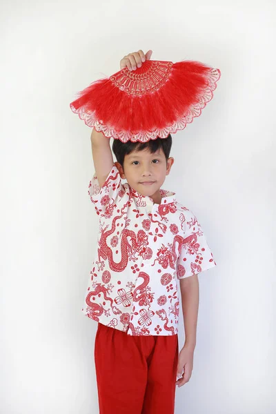 Geleneksel kırmızı ejderha desenli tişörtlü yakışıklı Asyalı çocuk Çin Yeni Yıl Festivali 'ni kutlamak için başının üstünde süslü kırmızı tüy yelpazesi tutuyor..