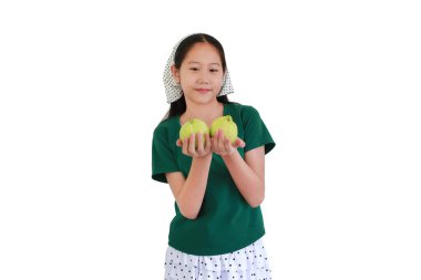Yeşil tişörtlü ve benekli başörtülü şirin bir kız elinde beyaz arka planda izole edilmiş iki taze guava tutarken gülümsüyor..