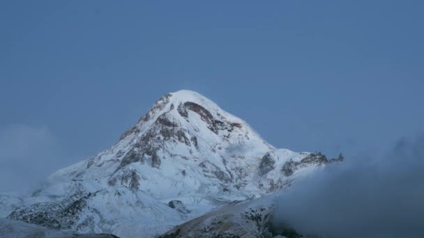 Stepantsminda, Gergeti, Georgia. Όρος Kazbek Καλυμμένο χιόνι το χειμώνα ανατολή. Πρωινή Αυγή Χρωματιστά κορυφή του βουνού σε ροζ χρώματα. Φοβερό τοπίο της φύσης. Χρόνος λήξης Timelapse 4K — Αρχείο Βίντεο