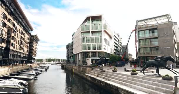 Oslo, Noruega - 24 de junho de 2019: Pessoas que caminham perto de casas residenciais de vários andares no distrito de Aker Brygge na noite de verão. Lugar famoso e popular. 4K — Vídeo de Stock