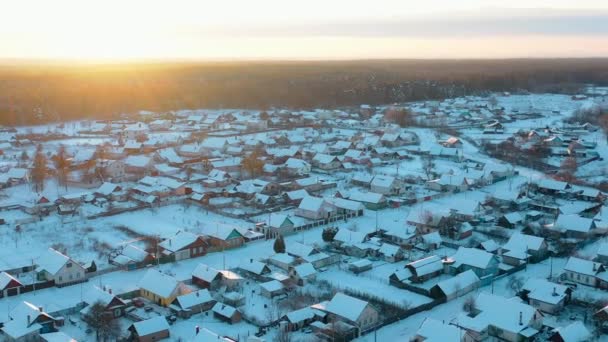 村の雪に覆われた菜園の空中ビュー。冬の夜のスカイライン。日没時に村のスカイラインの上に輝く太陽。ドブラシ、ゴメル地域、ベラルーシ。空中ビュータウンスカイライン。鳥 — ストック動画