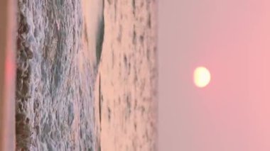 Denizin üstünde günbatımı güneşi. Dalgacık Denizi Üzerindeki Doğal Gökyüzü Sıcak Renkleri. Okyanus suyu köpüğü, gün batımında kumsalda yıkanır. Dikey.