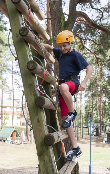A boy wearing a safety harness and a helmet walking in a rope park.