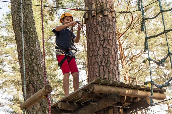 Een jongen die het dragen van een helm wandelen in een touwbaanparcours en een veiligheidsharnas. — Stockfoto