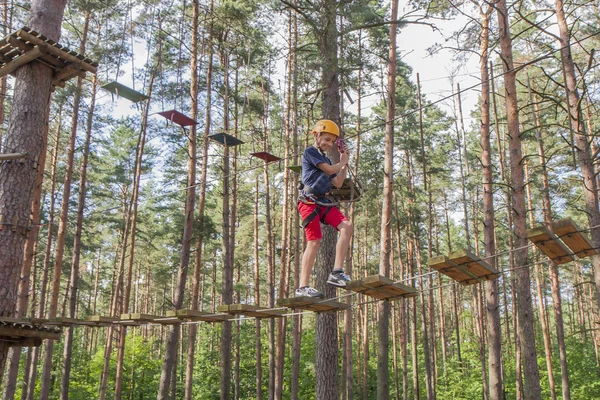 Un ragazzo con un'imbracatura di sicurezza e un casco che cammina in un parco di corde . — Foto Stock