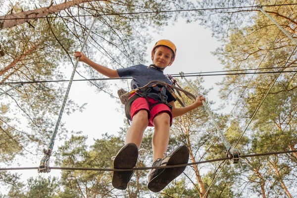 A boy wearing a safety harness and a helmet walking in a rope park.