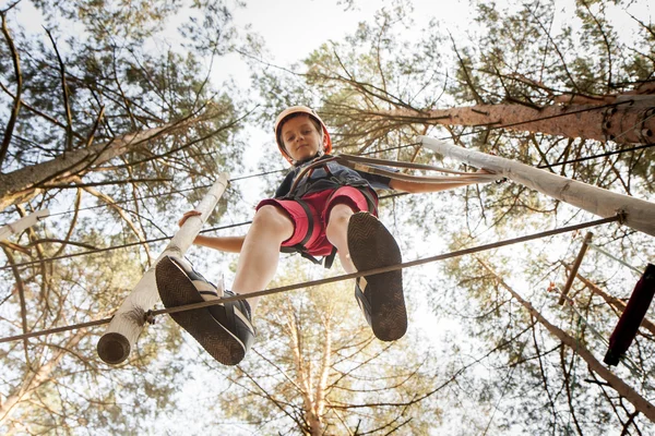 A boy wearing a safety harness and a helmet walking in a rope park. — Stock Photo, Image