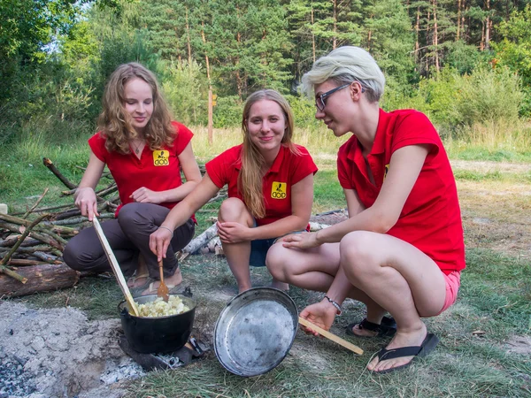 Tres chicas guapas jóvenes cocinan una comida en una olla en el picnic — Foto de Stock