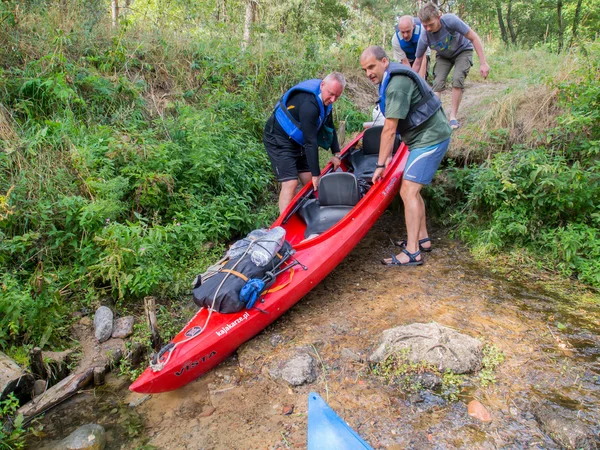 Um par de homens levantar uma canoa pesada descendo uma encosta para um rio — Fotografia de Stock