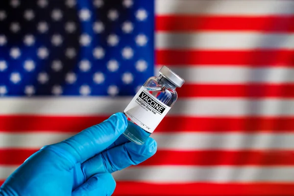 Doctor with a vial with doses of the vaccine in front of the US flag. Preparation of vaccine injection for the annual vaccination plan against diseases in the USA.