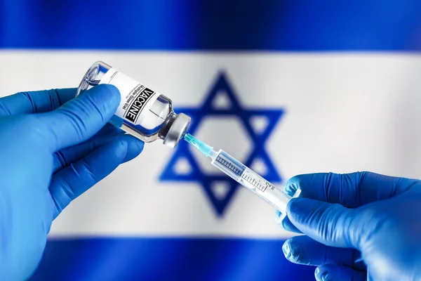Doctor preparing vial of vaccine injection for the vaccination plan against diseases in Israel. Preparing dose of vaccine in syringe for infections prevention in front of the Israel flag