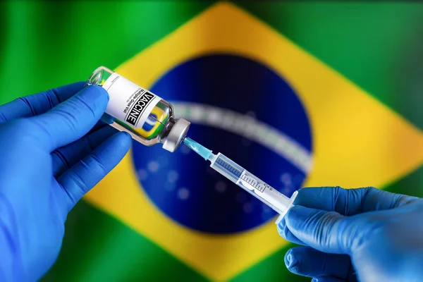 Doctor preparing vial of vaccine injection for the vaccination plan against diseases in Brazil. Preparing dose of vaccine in syringe for infections prevention in front of the Brazilian flag