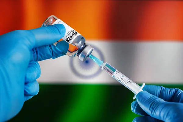 Doctor preparing vial of vaccine injection for the vaccination plan against diseases in India. Preparing dose of vaccine in syringe for infections prevention in front of the Indian flag