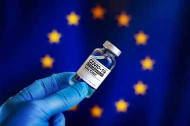 Avrupa ülkelerindeki hastalıklara karşı koronavirüs aşısı için bir şişe aşı. Covid-19 aşısı şişesi ve Avrupa Birliği 'nin arka plan bayrağını taşıyan bir doktor.