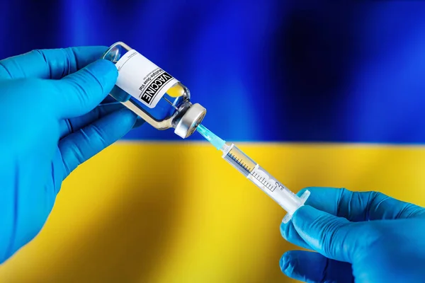 Doctor preparing vial of vaccine injection for the vaccination plan against diseases in Ukraine. Injecting dose of vaccine in syringe for infections prevention in front of the Ukrainian flag