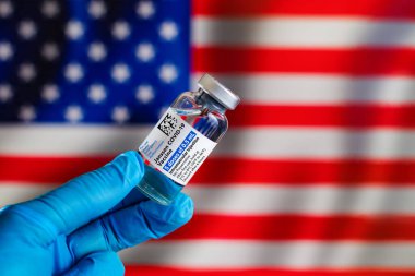 Madrid, Madrid, Spain - April 20, 2021. Vial of vaccine Janssen Johnson and Johnson for vaccination Coronavirus after the resolution of FDA in USA. Vial of the Janssen vaccine from the Johnson & Johnson company for Covid-19 in front of USA flag clipart